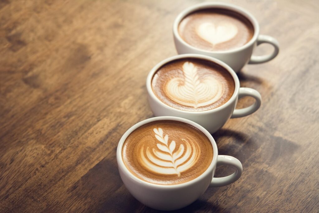 3 tasses de café disposées en diagonale avec sur le dessus une jolie déco faite par un'e barista